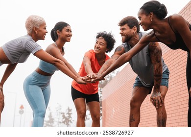 Group of smiling multi ethnic male and female athletes joining hands together before starting their urban workout routine, showing teamwork and motivation - Powered by Shutterstock