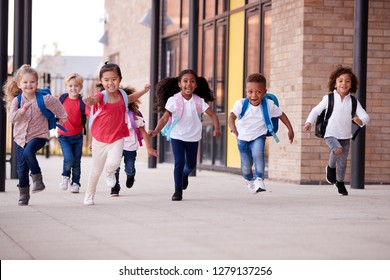 A group of smiling multi-ethnic school kids running in a walkway outside their infant school building after a lesson - Shutterstock ID 1279137256