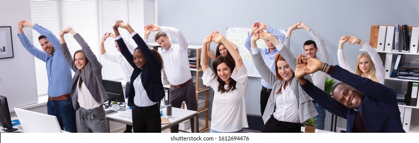 Group Of Smiling Multi-ethnic Young Office Workers Doing Stretching Exercise At Workplace