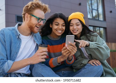 Group of smiling multiracial friends using mobile phone, watching video, shopping online, having fun outdoors.  Young happy students studying, learning language, communication together  - Powered by Shutterstock