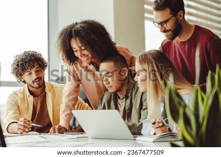 Group of smiling multiracial university students using laptop exam preparation studying together. Education concept. Young team, colleagues meeting, working, planning startup project in modern office 
