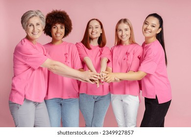 Group of smiling multiracial women wearing t shirts with breast cancer pink ribbon holding hands together isolated on pink background. Health care, support. Breast cancer awareness month concept - Powered by Shutterstock