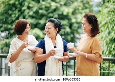 Group of smiling senior female friends drinking tea and discusing news when standing on big porch - Powered by Shutterstock