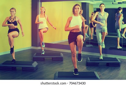 Group of smiling sporty women working out with steppers in fitness center