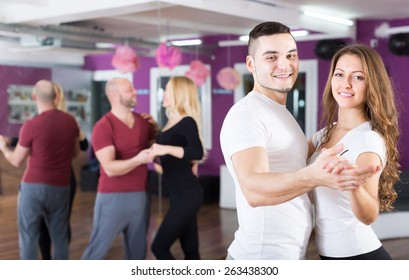 Group of smiling young adults dancing salsa at dance class. Focus on guy