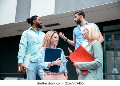 Group Of Smiling Young Diverse People With Laptop And Folders Talking In Front Of University Building