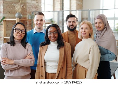 Group of smiling young interracial colleagues of modern company standing together in loft open space office