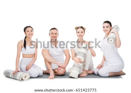 Group of smiling young women with trainer sitting together with yoga mats isolated on white