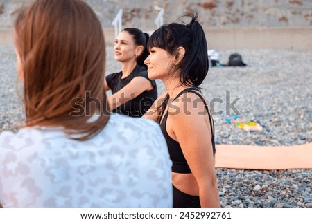 Group of smiling young-adult multi-racial women are sitting on sports mats on wild beach and talking to each other. Concept of female circle of communication and yoga class.