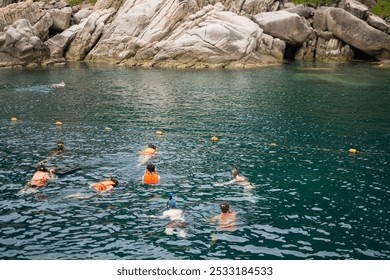 A group of snorkelers explores the clear, turquoise waters near rocky cliffs, eager to discover the underwater world. - Powered by Shutterstock