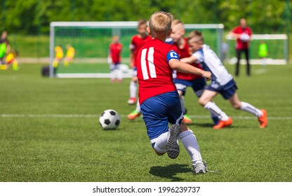 Group Of Soccer Boys In Red Uniforms Playing School Tournament Game. Child Football Team Captain Running Ball And Compete In A Duel