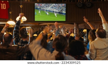 Group of Soccer Fans Cheering, Screaming, Raising Hands and Jumping During a Football Game Live Broadcast in a Sports Pub. Player in Blue Shirt Scores a Goal and Friends Celebrate. Slow Motion Footage