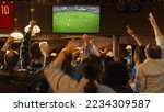 Group of Soccer Fans Watching a Live Football Match in a Sports Bar. People Standing in Front of a TV, Cheering for Their Team. Player Scores a Goal and Crowd Celebrate Winning the Championship.