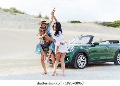 A Group Of Spanish Friends On The Beach, Having Fun And Jumping On Each Other's Backs In Front Of Their Luxury Car