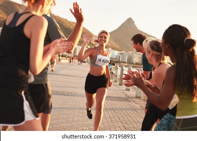 Group of spectators cheering runners just before the finish line. Female runner finishing the race with her team applauding her efforts. - Powered by Shutterstock