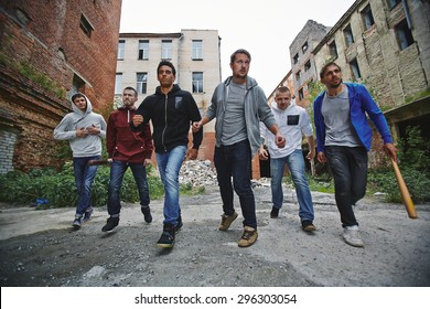 Group of spiteful hooligans walking along grunge brick houses - Shutterstock ID 296303054