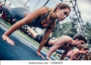 Group Of Sports People Are Training Outdoors With TRX. Total Body Resistance Exercises. Two Attractive Young Women And Handsome Man Are Working Out In Gym.