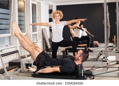 Group of sporty and athletic people are working out Pilates exercises with instructor on special equipment in modern studio interior. Fitness, sport, training and people concept - Powered by Shutterstock