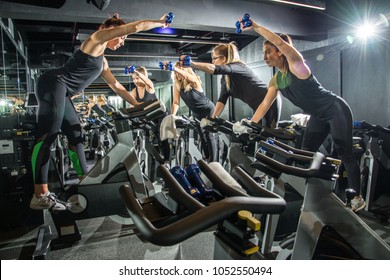 Group Of Sporty Girlfriends Training Together With Dumbbells On Cycling Class At Gym.