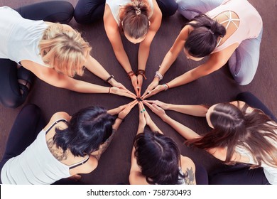 Group of sporty happy people sitting on the gym floor in a circle together, resting and meditating after yoga class, talking about healthy life with instructor indoors. Healthy lifestyle concept