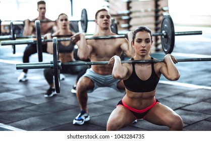 Group of sporty muscular people are working out in gym. Cross fit training. Handsome shirtless men and attractive women are doing exercises with barbells. Weightlifting. - Powered by Shutterstock