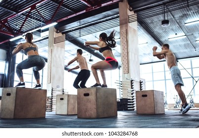 Group Of Sporty Muscular People Are Working Out In Gym. Cross Fit Training. Jumping On A Box Together.