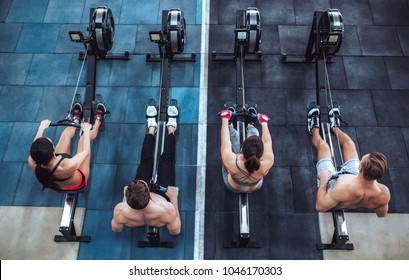 Group of sporty muscular people are working out in gym. Cross fit training. Paddling training apparatus. Top view of four sportsmen are rowing together. - Shutterstock ID 1046170303