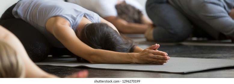 Group sporty people practice Child Balasana pose exercise lying on mats at yoga training with instructor in club, wellbeing bodycare concept, banner for website header design with copy space for text