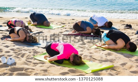 Group of sporty people practicing various yoga positions during training on beach