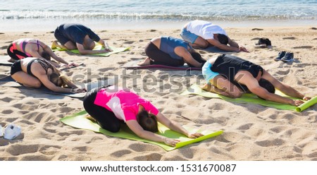 Group of sporty people practicing various yoga positions during training on beach