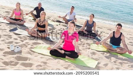 Group of sporty people practicing yoga in lotus positions on ocean beach
