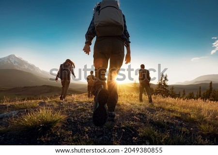 Group of sporty people walks in mountains at sunset with backpacks. Altai mountains, Siberia, Russia.