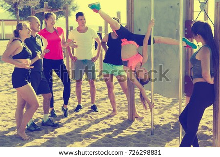 Group of sporty people watching for girl doing exercises on pole