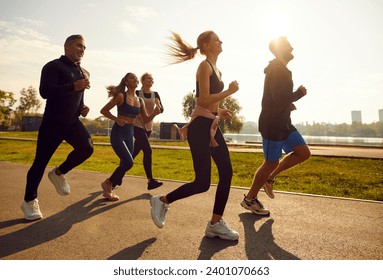 Group of sporty smiling people in sportswear jogging together in the park at sunset. Friends running outdoor having sport training in nature. Team of runners on workout. Sport and fitness concept. - Powered by Shutterstock