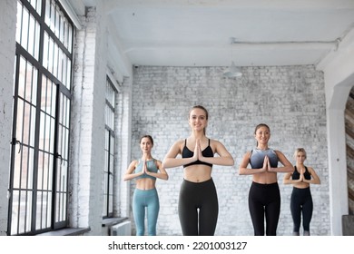 Group Of Sporty Women Doing Yoga Exercises In Gym Prayer Position Beautiful Slim Girls Wearing Sportswear Posing At Grey Fitness Center Wall Background.