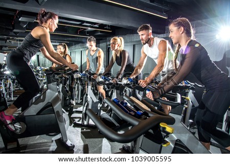 Group of sporty women and men training on exercise bikes together at gym.