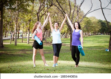 Group sporty women of mother and her daughter standing with mat in yoga sport uniform rejoice raising their hands up after exercise in outdoor class. Team, friendship and helthy lifestyle concept.