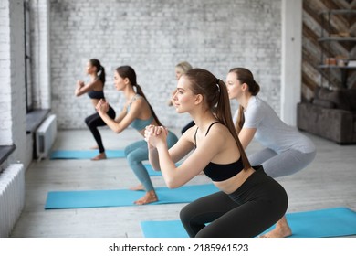 Group Of Sporty Women On Yoga Mats Doing Fitness Or Yoga Exercises In Gym, Beautiful Slim Girls Wearing Sportswear Posing At Grey Fitness Center Wall Background.