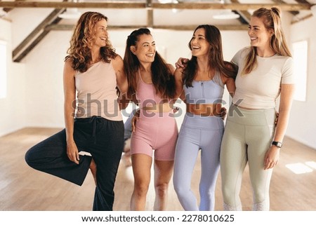Group of sporty women smiling happily while standing together in a yoga studio. Cheerful female friends working out together in a fitness studio. Women of different ages attending a yoga class.