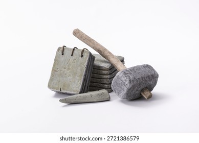 A group of stone objects on a white background, including stone tablets, a stone chisel, and a stone hammer, arranged as a conceptual still-life composition.