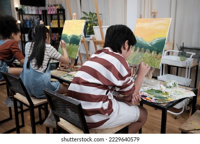 A group of student kids concentrates on acrylic color picture painting with a paintbrush on canvas in art classroom, creatively learning with talents and skills at elementary school studio education.  - Powered by Shutterstock