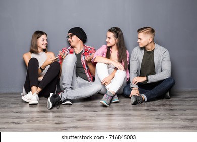 Group of students in casual clothes using gadgets, talking and smiling while sitting together on the floor