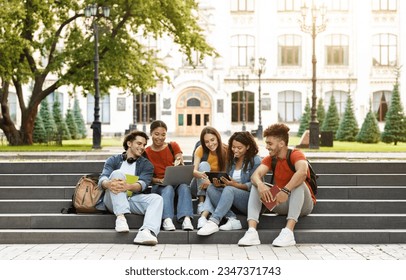 Group Of Students With Digital Tablet And Laptop Study Together Outdoors, Happy Multiethnic Young Friends Sitting On Stairs Near University Building, Using Modern Gadgets For Education, Copy Space