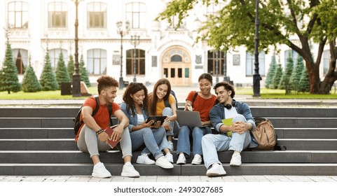 Group Of Students With Digital Tablet And Laptop Study Together Outdoors, Happy Multiethnic Young Friends Sitting On Stairs Near University Building, Using Modern Gadgets For Education, Copy Space - Powered by Shutterstock