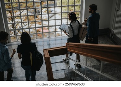 A group of students engage in a discussion while descending a staircase. They are carrying backpacks and holding study materials, highlighting a collaborative learning environment.