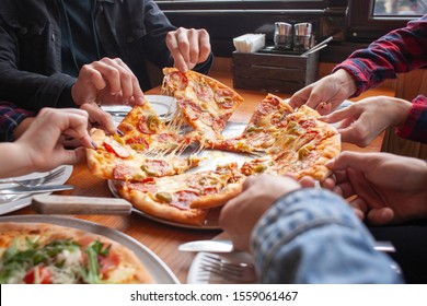 group of students friends eat Italian pizza, hands take slices of pizza in a restaurant, close-up - Powered by Shutterstock