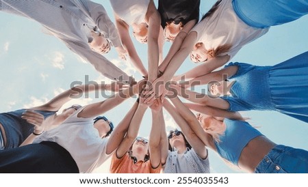 Group of students joining hands together in circle against blue sky, celebrating graduation day