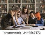 Group of students leaned at desk full of textbook and study materials, discuss joint task, share opinion, learn subject, work on essay, think of solution gathered in university of high-school library