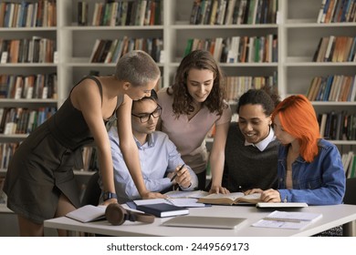 Group of students leaned at desk full of textbook and study materials, discuss joint task, share opinion, learn subject, work on essay, think of solution gathered in university of high-school library - Powered by Shutterstock