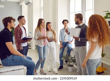 Group of students listening a professor explaining something and showing a book. They are standing around teacher lector and listening him. Education at highschool, college, university concept. - Shutterstock ID 2195309519